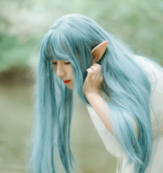 A young woman with long blue hair and pointed elf ears in a white dress, beside a forest stream.